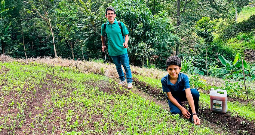 Eddy, sonriendo, enseña a su hijo a aplicar el producto M5, un biopesticida de su propia creación, en un cultivo.