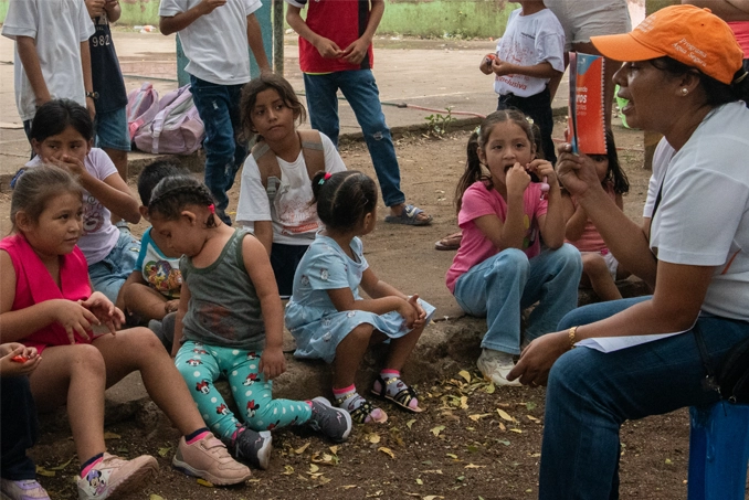 Un grupo de niños sentados mientras escuchan un cuento siendo leído por una especialista de la organización.